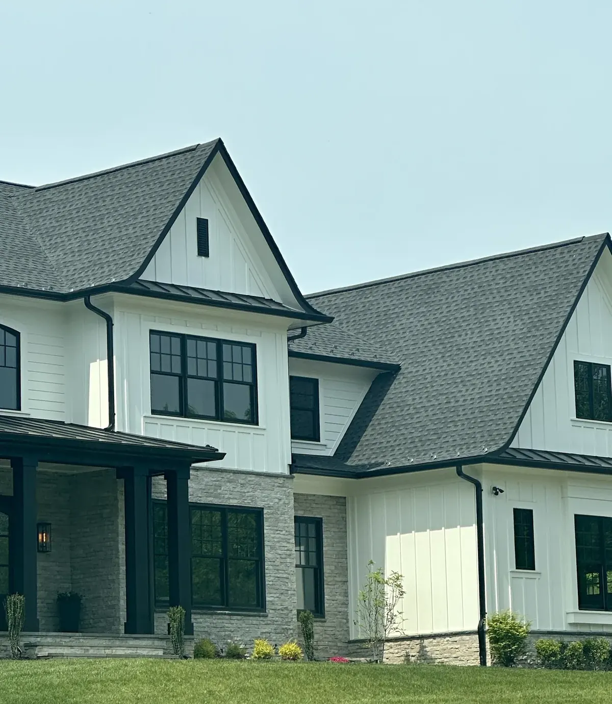Two story white house with a gray shingle roof and dark metal porch roofs