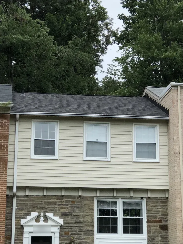 Townhouse with a dark gray shingle roof above beige siding and a brick end wall